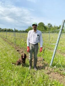 Photo shows Adrian standing in front of vines with a brown cocker spaniel sat down next to him